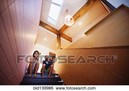 Mixed race children using cell phones on staircase View Large Photo Image Stock Photograph - Mixed race children using cell phones on staircase. Fotosearch