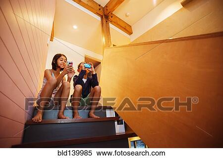 Stock Photography - Mixed race children using cell phones on staircase. Fotosearch