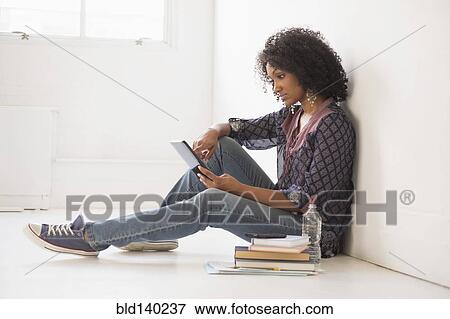 Stock Photo - Mixed race college student using digital tablet on floor. Fotosearch