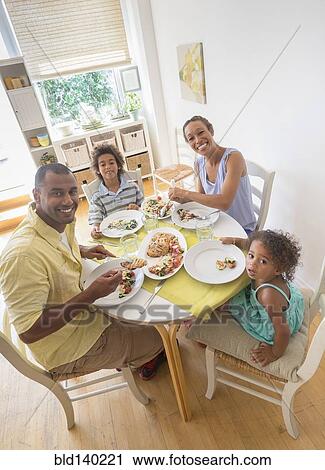 Stock Image - Mixed race family smiling at dining room table. Fotosearch