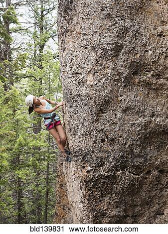 Stock Image - Mixed race girl climbing steep cliff. Fotosearch