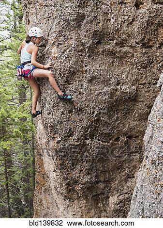 Stock Image - Mixed race girl climbing steep cliff. Fotosearch
