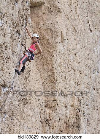 Stock Photo - Mixed race girl climbing steep cliff. Fotosearch