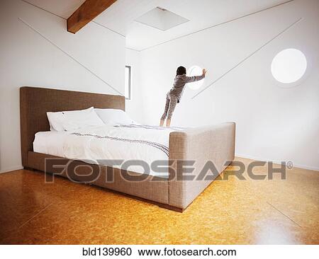 Stock Image - Mixed race girl looking out window in modern bedroom. Fotosearch
