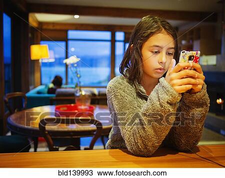 Stock Image - Mixed race girl using cell phone at table. Fotosearch