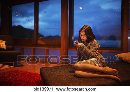 Stock Image - Mixed race girl using cell phone in living room. Fotosearch