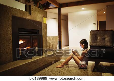 Stock Photo - Mixed race girl using cell phone near fireplace in living room. Fotosearch