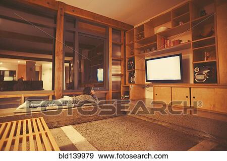 Stock Photo - Mixed race girl watching television in modern living room. Fotosearch