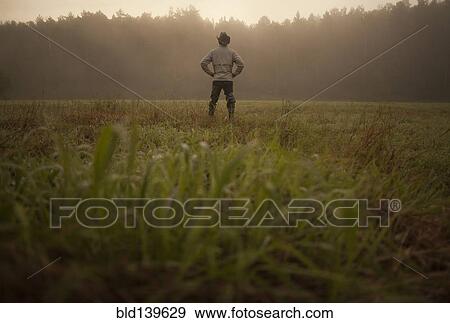 Stock Photo - Mixed race man standing in field in rural landscape. Fotosearch