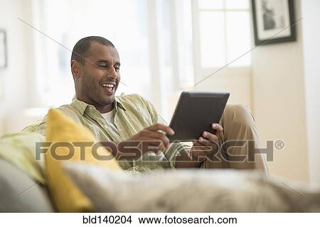 Picture - Mixed race man using digital tablet in living room. Fotosearch