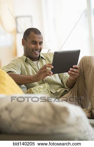 Stock Photography - Mixed race man using digital tablet in living room. Fotosearch