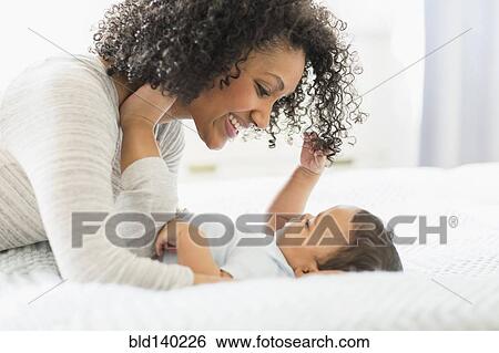 Stock Photograph - Mixed race mother holding baby on bed. Fotosearch