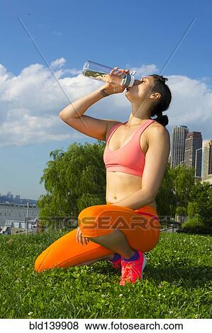 Stock Photo - Mixed race woman drinking water in urban park. Fotosearch