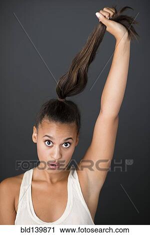 Stock Image - Mixed race woman pulling her ponytail. Fotosearch