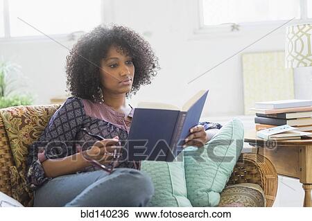 Stock Photograph - Mixed race woman reading book in living room. Fotosearch