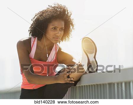 Stock Photo - Mixed race woman stretching leg on railing. Fotosearch