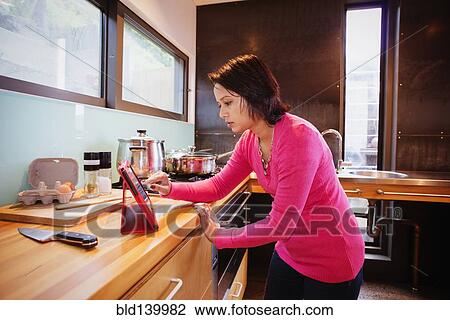 Stock Image - Mixed race woman using digital tablet in kitchen. Fotosearch