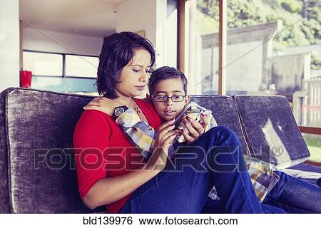 Stock Photograph - Mother and son using cell phone in living room. Fotosearch