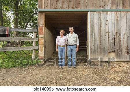 Stock Photography - Older Caucasian couple standing by barn on farm. Fotosearch