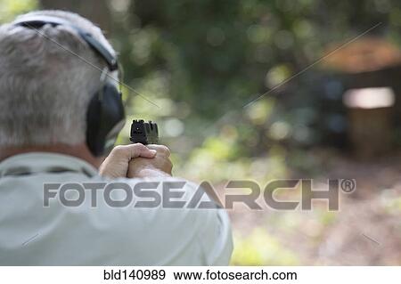 Stock Photo - Older Caucasian man practicing with gun at shooting range. Fotosearch