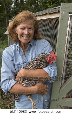 Stock Image - Older Caucasian woman holding chicken near coop. Fotosearch