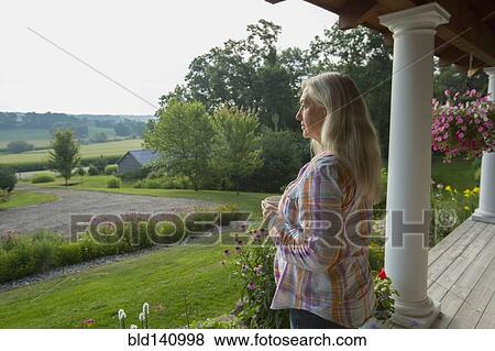Stock Photo - Older Caucasian woman overlooking rural scene from porch. Fotosearch