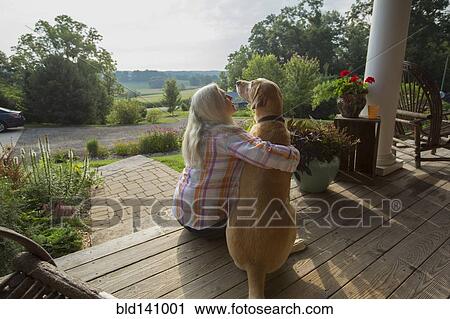 Stock Image - Older Caucasian woman petting dog on front porch. Fotosearch