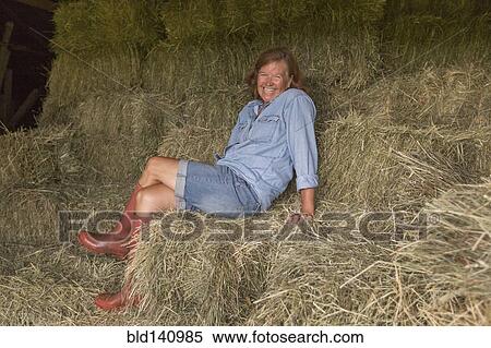 Stock Photography - Older Caucasian woman sitting on hay bales. Fotosearch