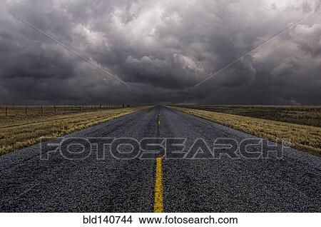 Picture - Paved road under cloudy sky in remote landscape. Fotosearch