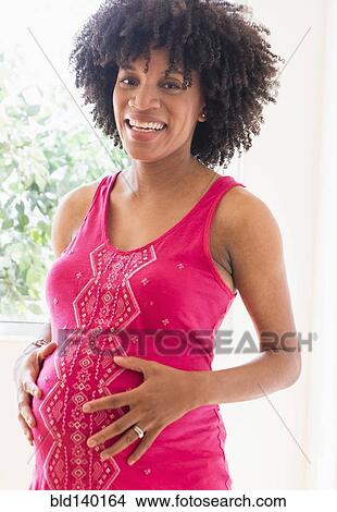 Picture - Pregnant African American mother holding her stomach. Fotosearch