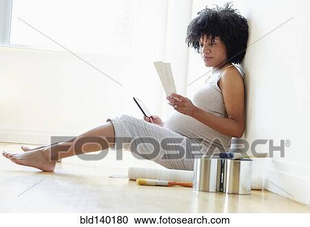 Stock Image - Pregnant African American mother examining paint swatches for nursery. Fotosearch