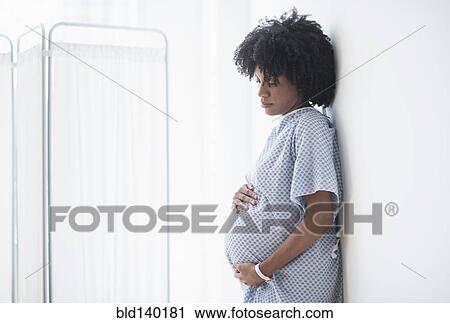 Stock Image - Pregnant African American mother holding stomach in hospital. Fotosearch