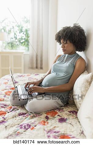 Picture - Pregnant African American mother using laptop computer in bed. Fotosearch