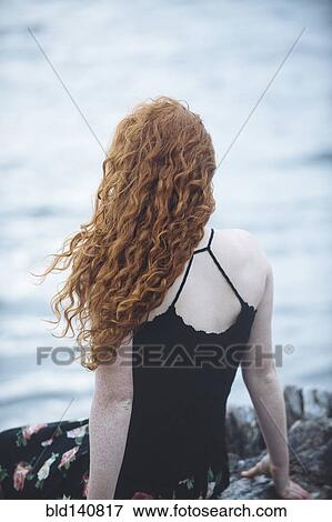Stock Photo - Rear view of girl sitting on beach. Fotosearch