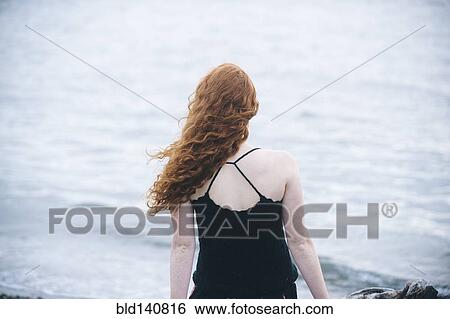 Stock Photograph - Rear view of girl sitting on beach. Fotosearch