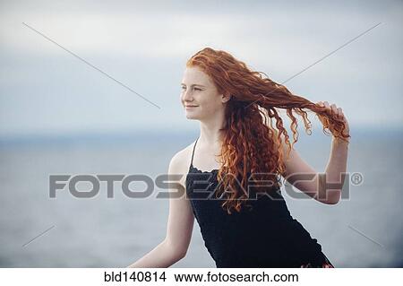 Picture - Red haired girl playing with hair on beach. Fotosearch