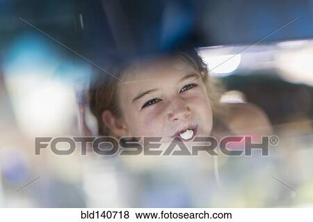 Stock Photo - Reflection of Caucasian girl blowing bubble gum bubble in rearview mirror. Fotosearch