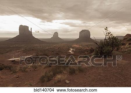 Picture - Rock formations in desert under cloudy sky, Monument Valley, Utah, United States. Fotosearch