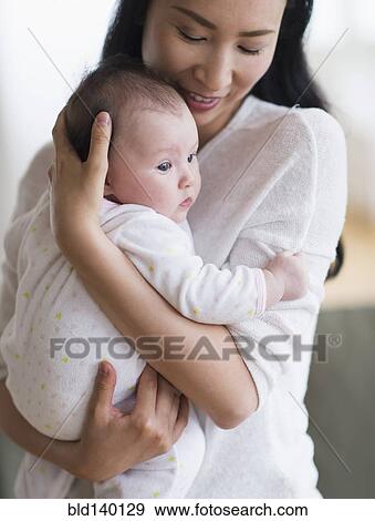 Smiling Asian mother holding baby View Large Photo Image Stock Photo - Smiling Asian mother holding baby. Fotosearch