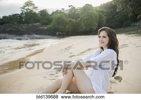Stock Photo - Smiling Caucasian woman sitting on beach. Fotosearch