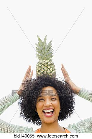 Stock Photography - Smiling woman balancing pineapple on head. Fotosearch