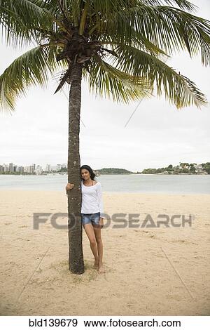 Stock Photo - Smiling woman hugging palm tree on tropical beach. Fotosearch