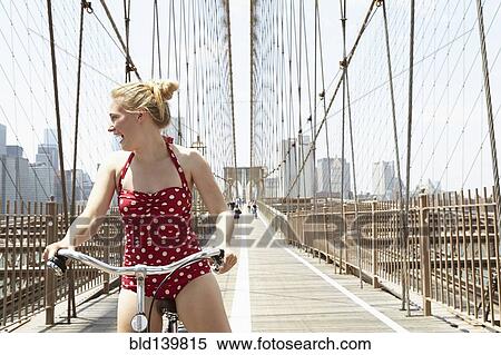 Stock Photography - Smiling woman riding bicycle across urban bridge, New York, New York, United States. Fotosearch