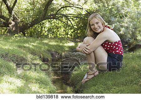 Stock Photo - Smiling woman sitting near creek in park. Fotosearch
