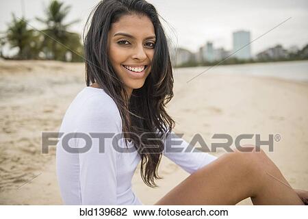 Stock Image - Smiling woman sitting on urban beach. Fotosearch