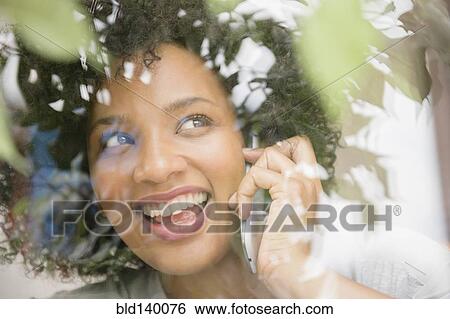 Stock Photograph - Smiling woman talking on cell phone near window. Fotosearch