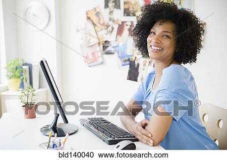 Stock Image - Smiling woman using computer at desk. Fotosearch