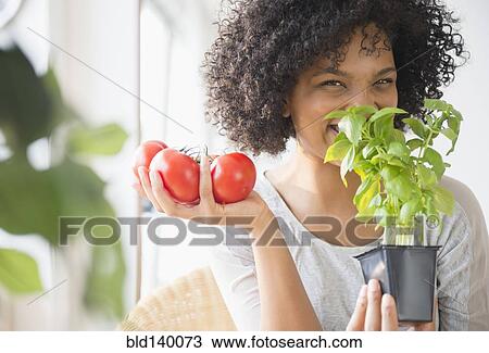 Stock Image - Smiling woman with tomatoes smelling plant. Fotosearch