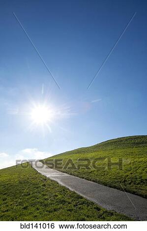 Sun shining over paved road on grassy hillside View Large Photo Image Stock Photograph - Sun shining over paved road on grassy hillside. Fotosearch
