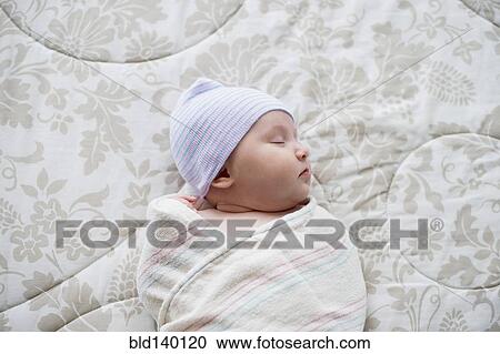 Stock Image - Swaddled Asian baby sleeping on bed. Fotosearch